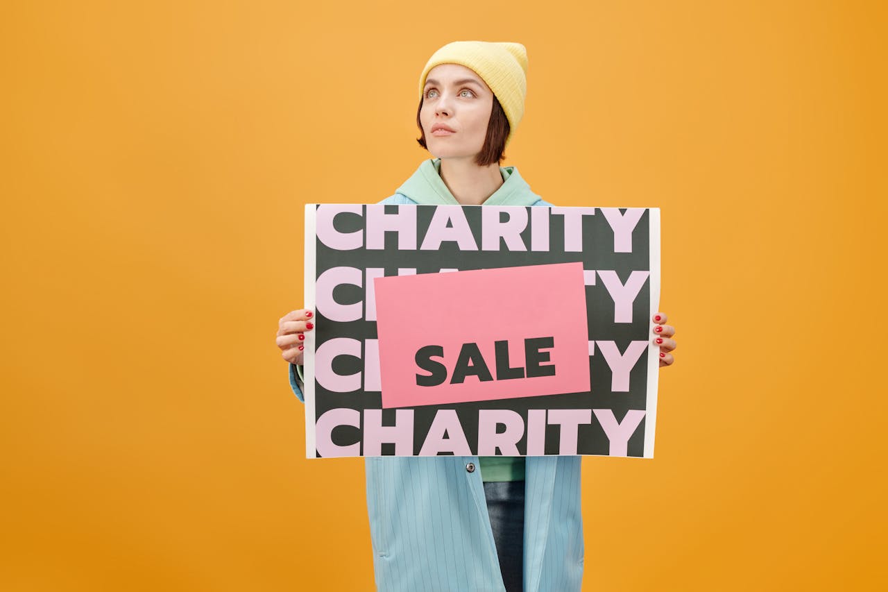 Woman in trendy outfit holding a charity sale sign against a vibrant yellow background.